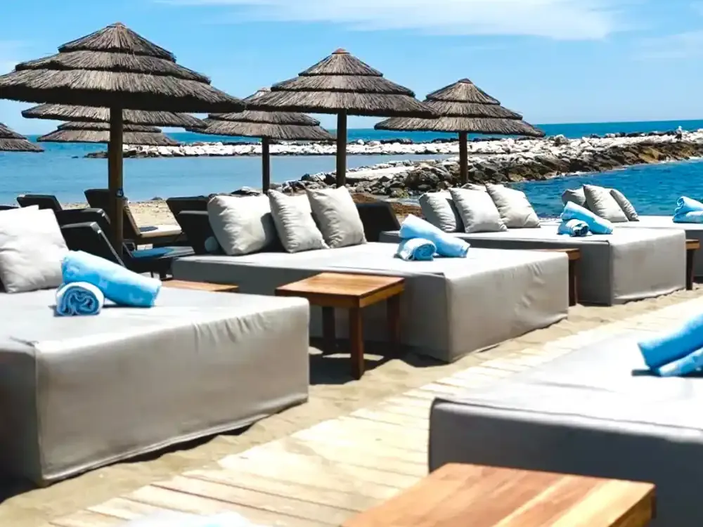 Camas de playa con cojines blancos y sombrillas de brezo frente al mar en Mistral Beach