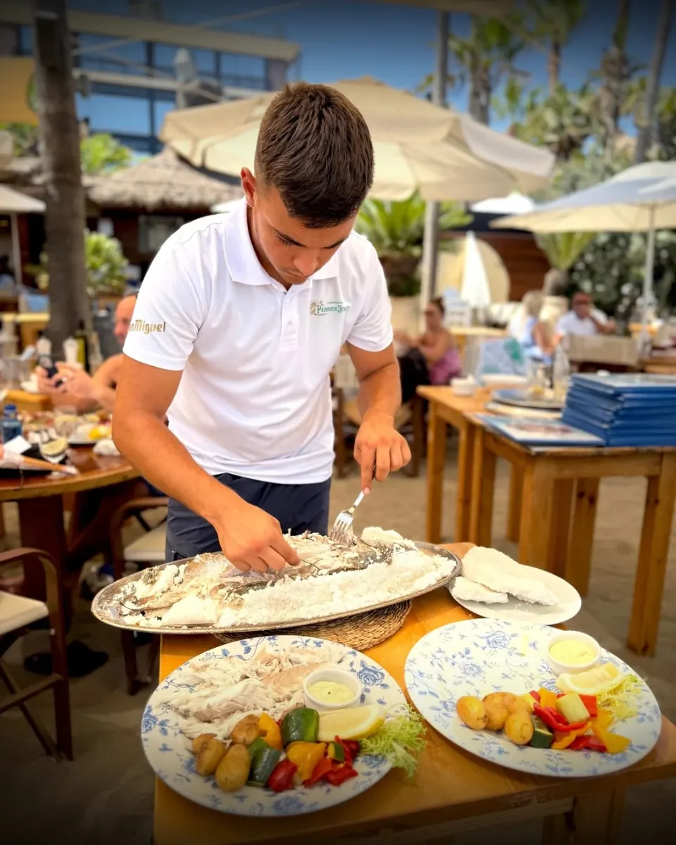 Camarero de Mistral Beach sirviendo pescado en la mesa de la terraza